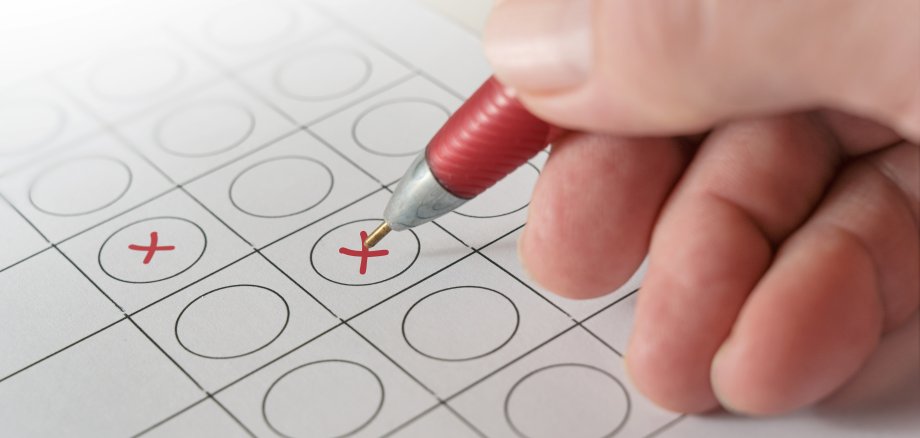 Hand holding a red ballpoint pen and makes crosses on a ballot paper, voting and election concept, copy space, selected focus